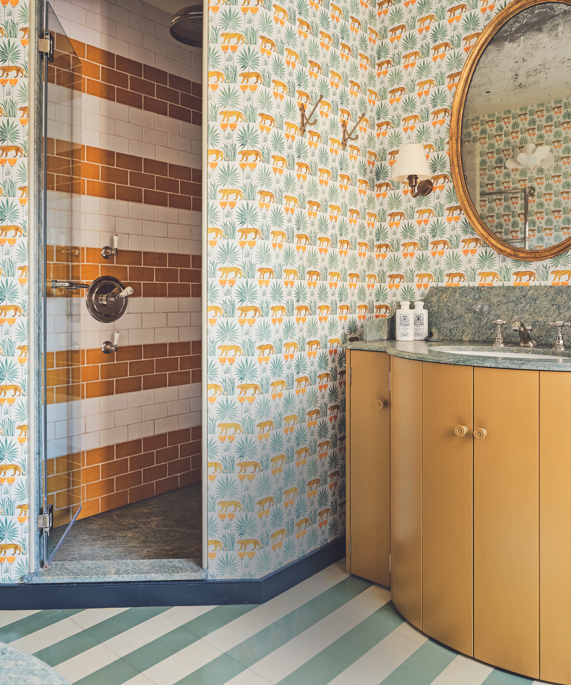 salle de bains avec beaucoup de motifs, y compris un sol à rayures et un papier peint à motifs de tigre dans une zone de douche carrelée à rayures dans des tons oranges, verts et bleus