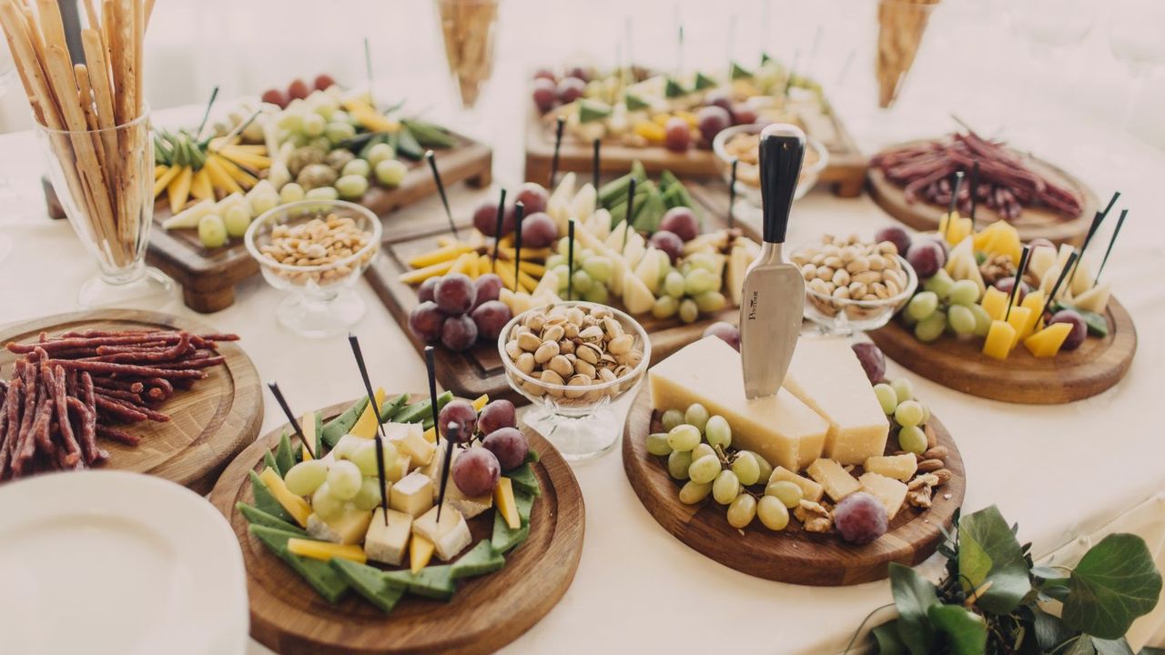 A layout of picking food such as ham crackers and cheese on wooden chopping boards on a white table