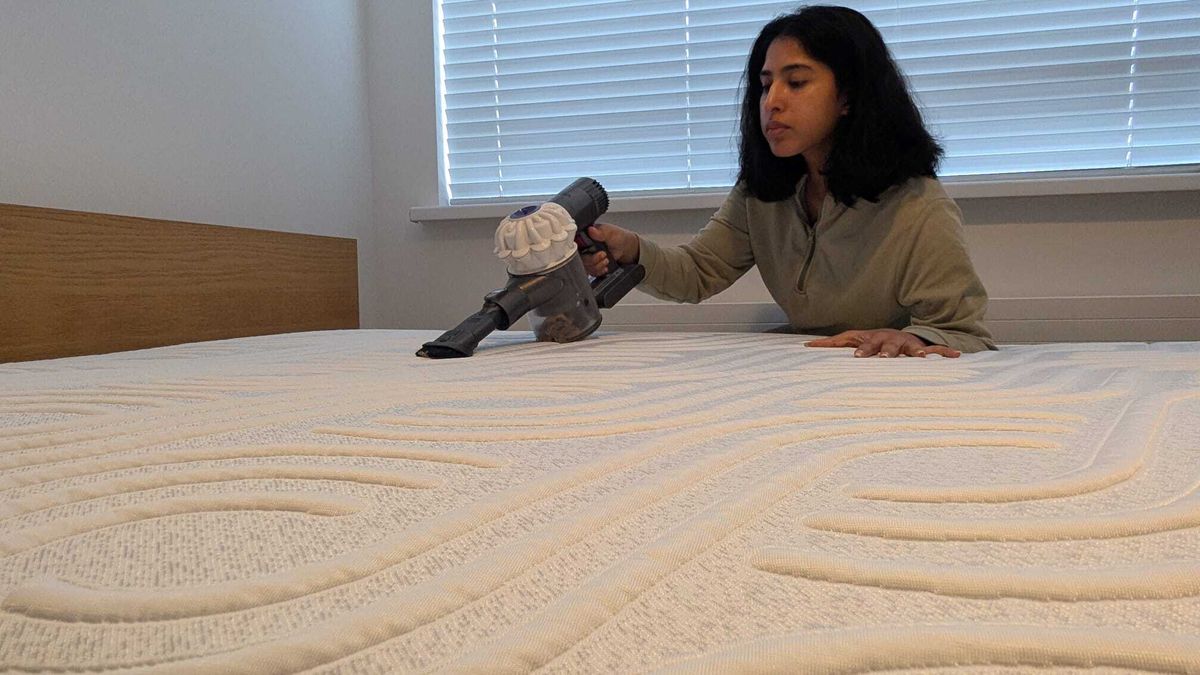The image shows a dark haired woman vacuuming a white mattress to remove dust mites