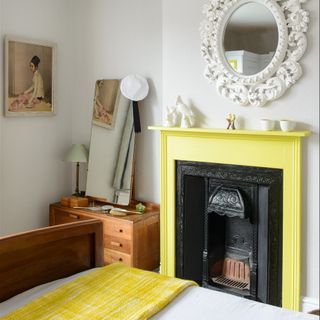 A white bedroom with a contrasting yellow-painted fireplace with a coordinating yellow throw on the bed