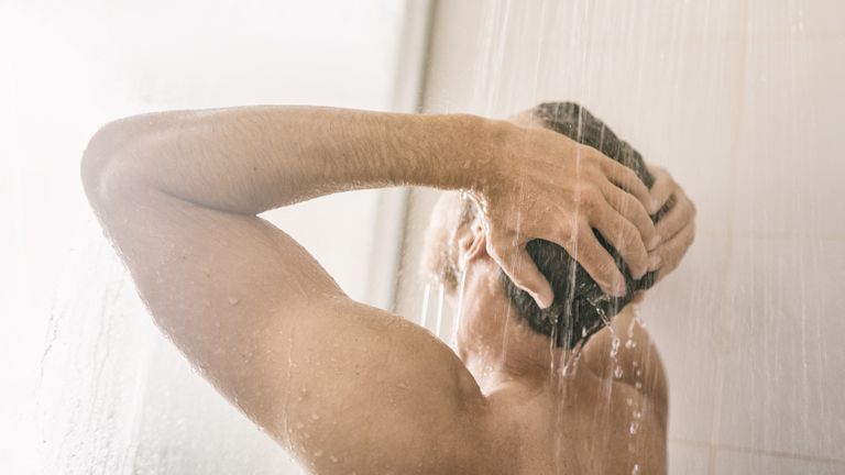A man standing in the shower, washing his hair with the best shampoo for men