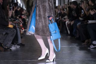 A model walks down the Tory Burch runway in a blue dress with a coordinating blue bag