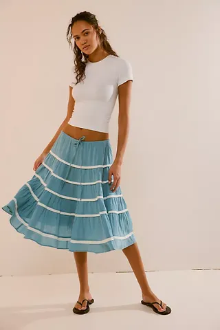 The model is wearing a white T-shirt and a blue striped low-rise skirt