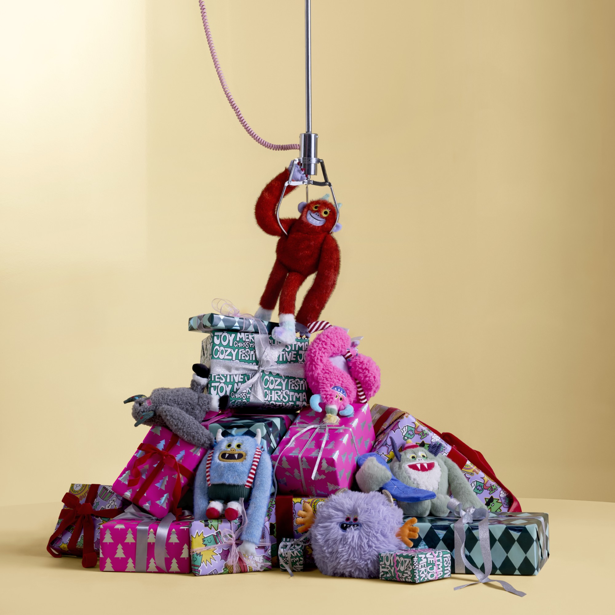 A pile of Christmas presents and Yeti toys and decorations from John Lewis on a butter yellow background