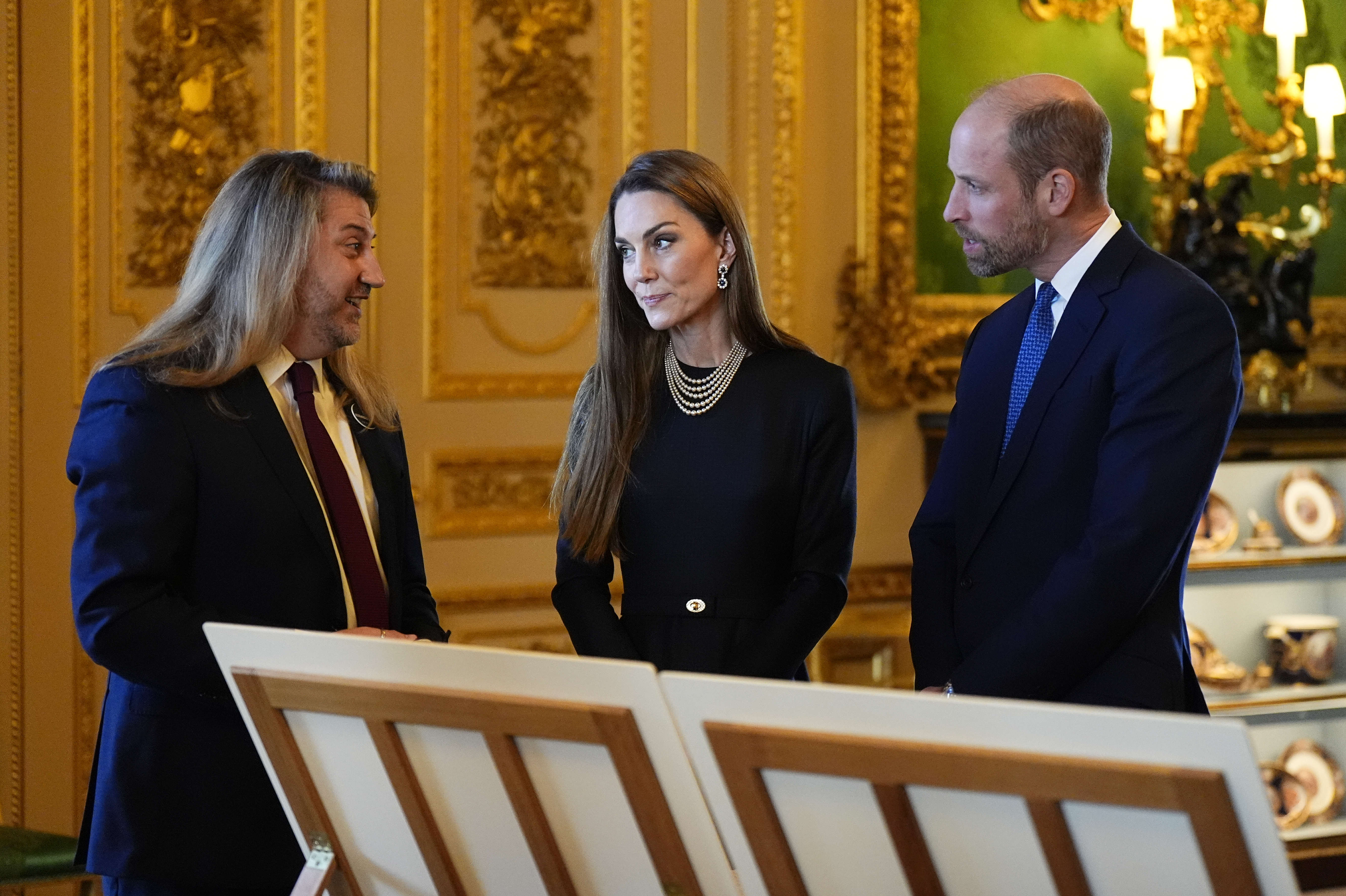 Princess Kate and Prince William talking to a man next to easels with artwork