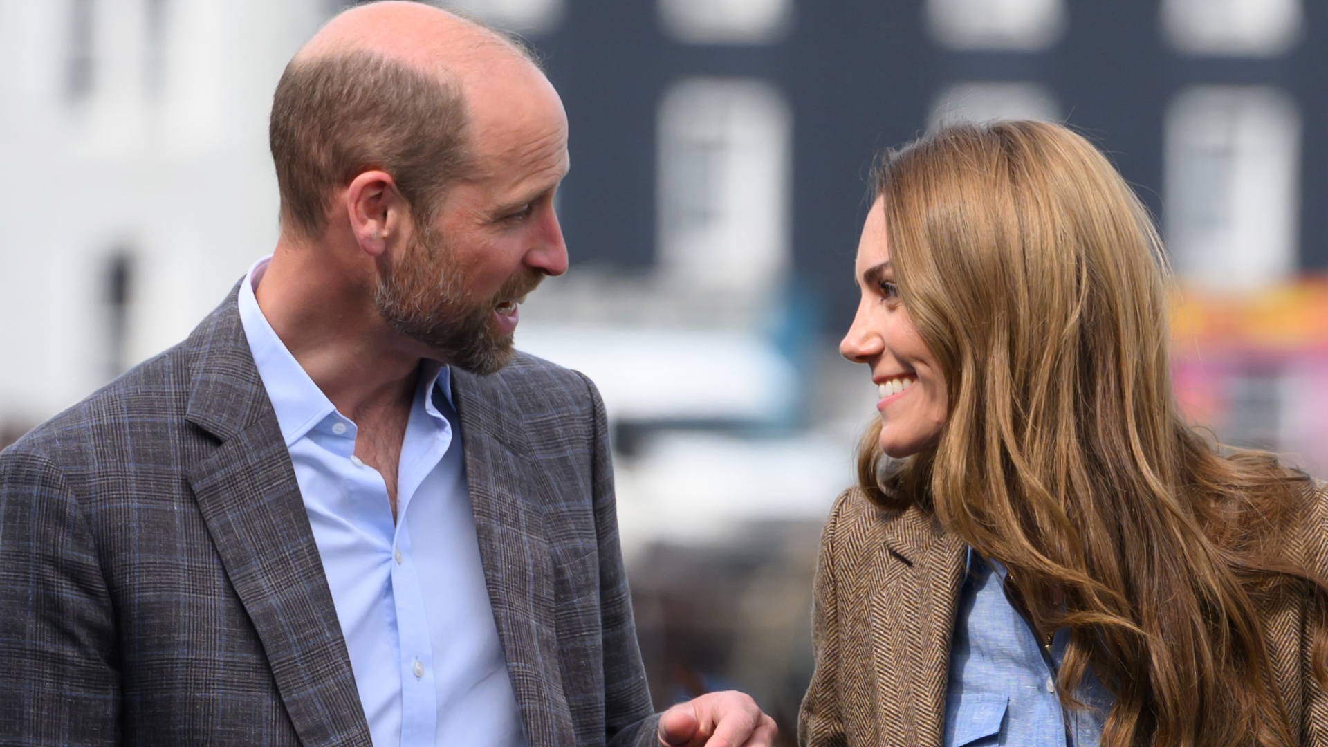 Prince William and Kate Middleton wearing blazers smiling at each other