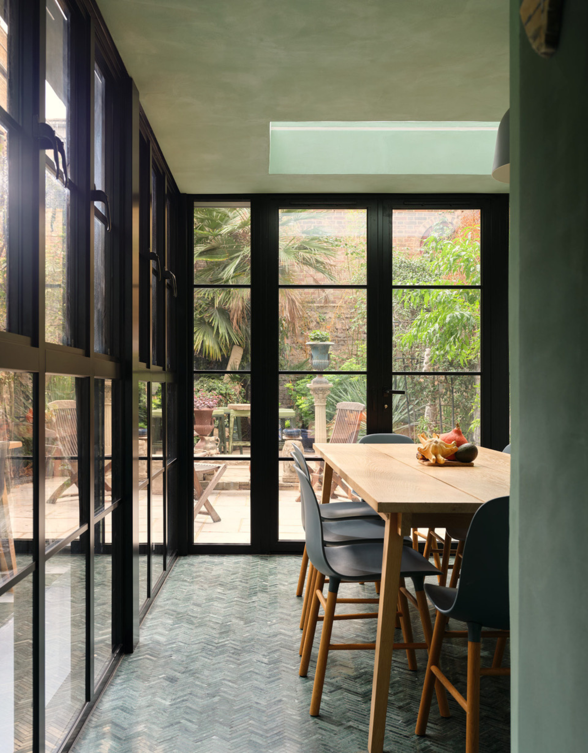 An aquamarine dining room with black doors, a wood table, and a set of chairs