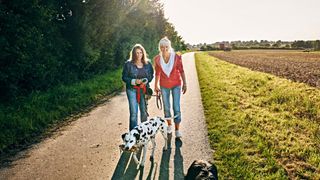 Two women walking with dogs along countryside road