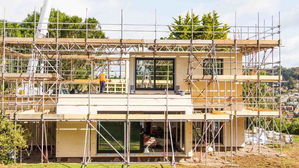 A package home under construction in the UK. The new build is surrounded by scaffolding, and there is a large crane in the background.