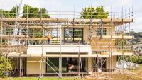 A package home under construction in the UK. The new build is surrounded by scaffolding, and there is a large crane in the background.