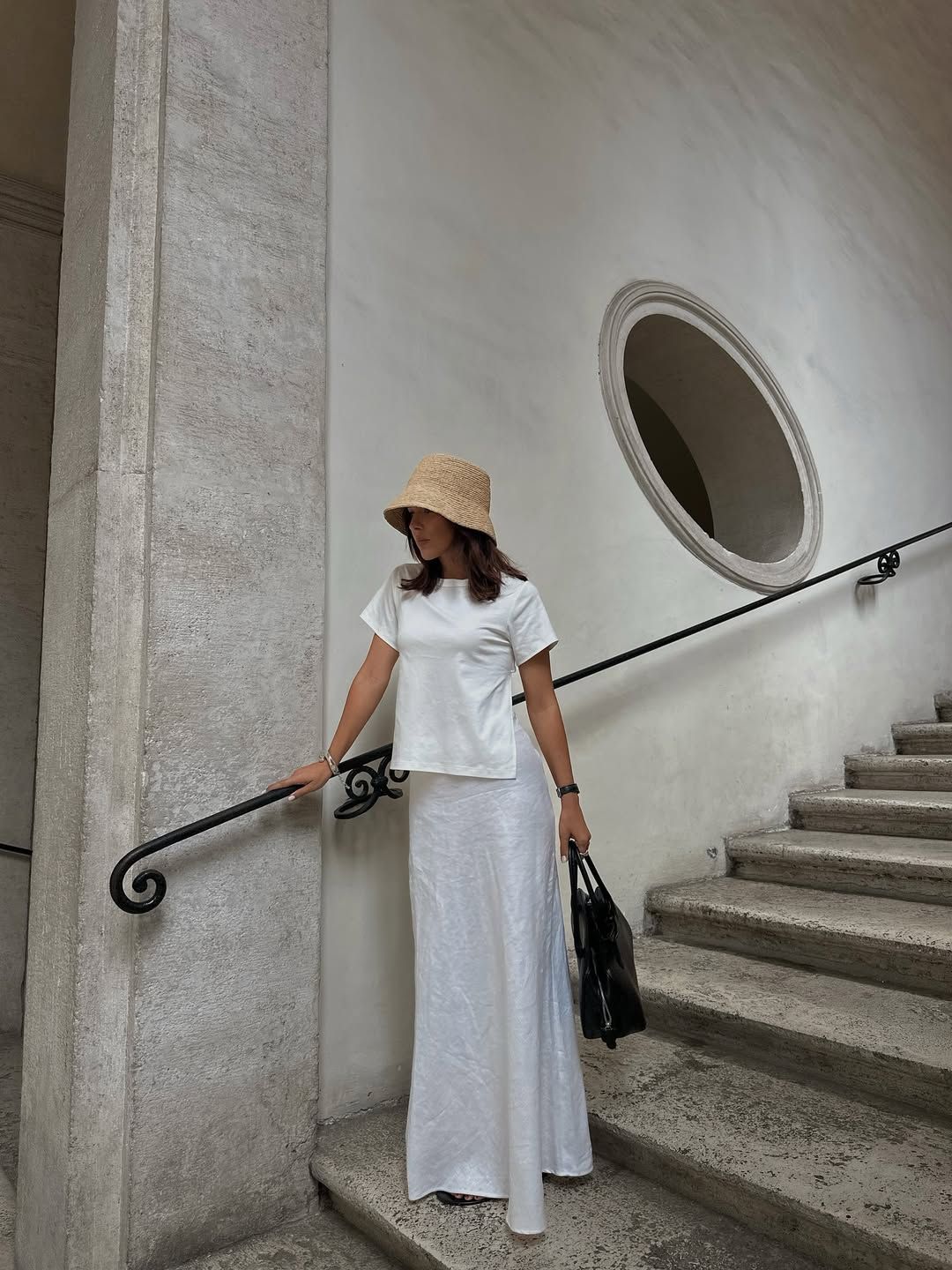 @deborabrosa wears a straw bucket hat with a white t-shirt, maxi skirt and black bag