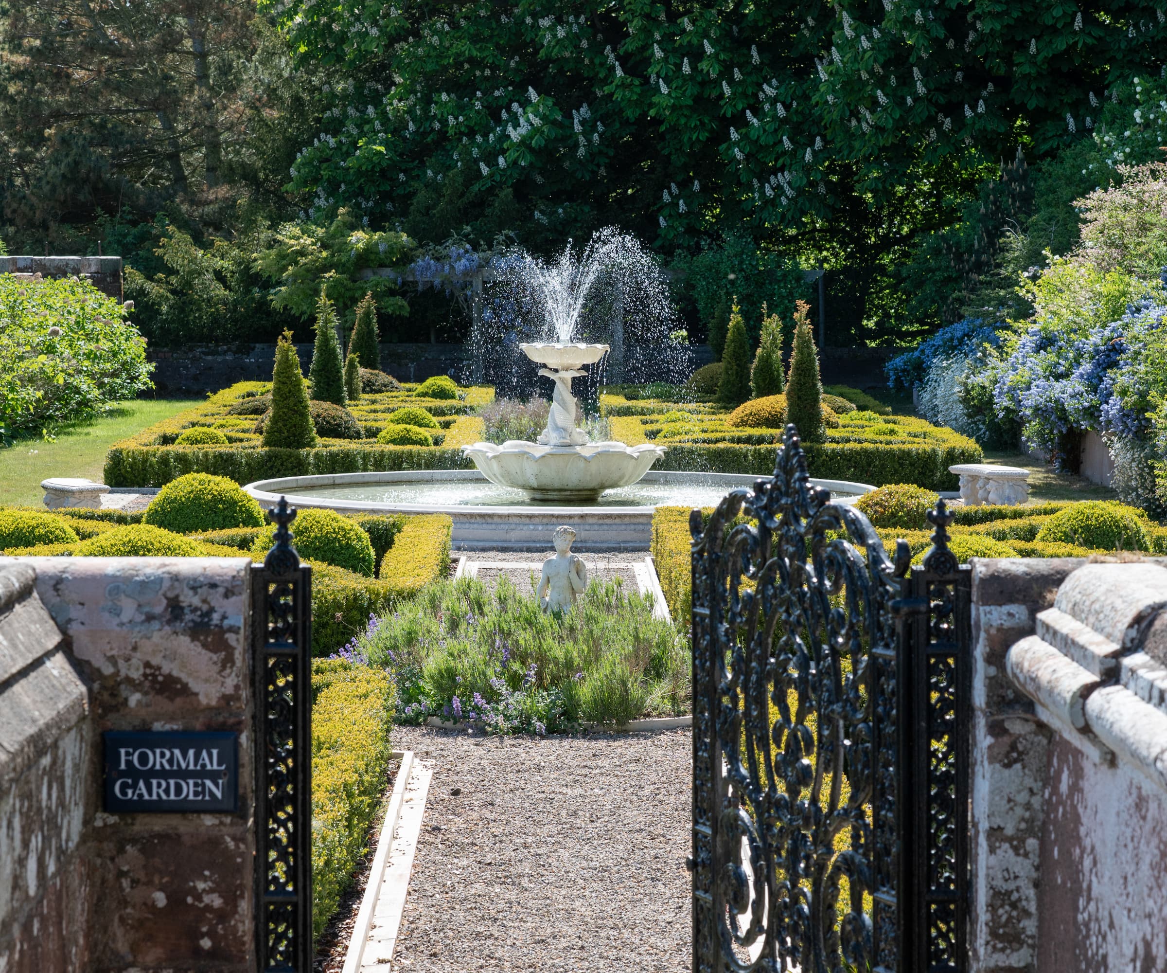 A fountain in the middle of a garden behind a gated wall