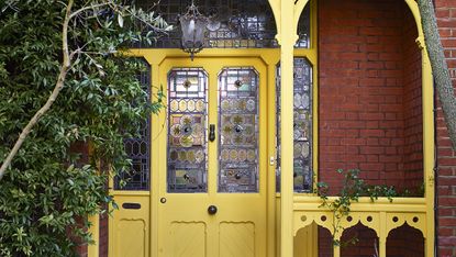 Yellow painted front door behind a Victorian style porch