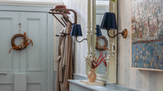a small entryway with a blue painted door and a wreath hanging on it, a small coat hook mounted to the wall, and two sconces on either side of a full length mirror 
