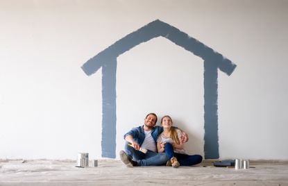 Happy couple sitting in the shape of a house painted on a wall