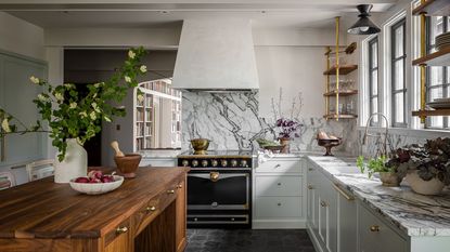 A light blue kitchen with marble countertops and a wooden island