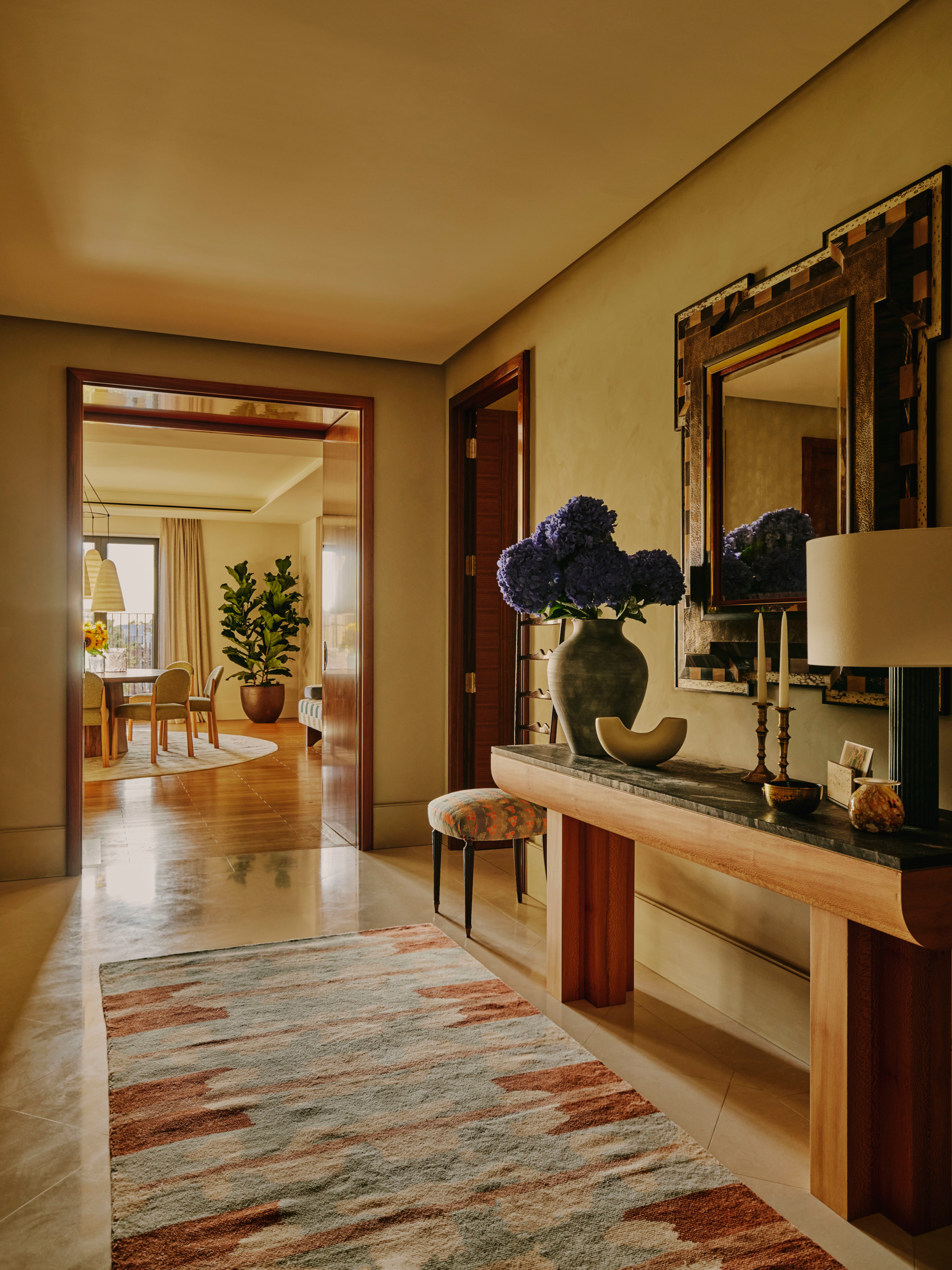 Ochre-painted hallway with wood and green marble-toped console, large checkerboard mirror and blue and rust abstract runner