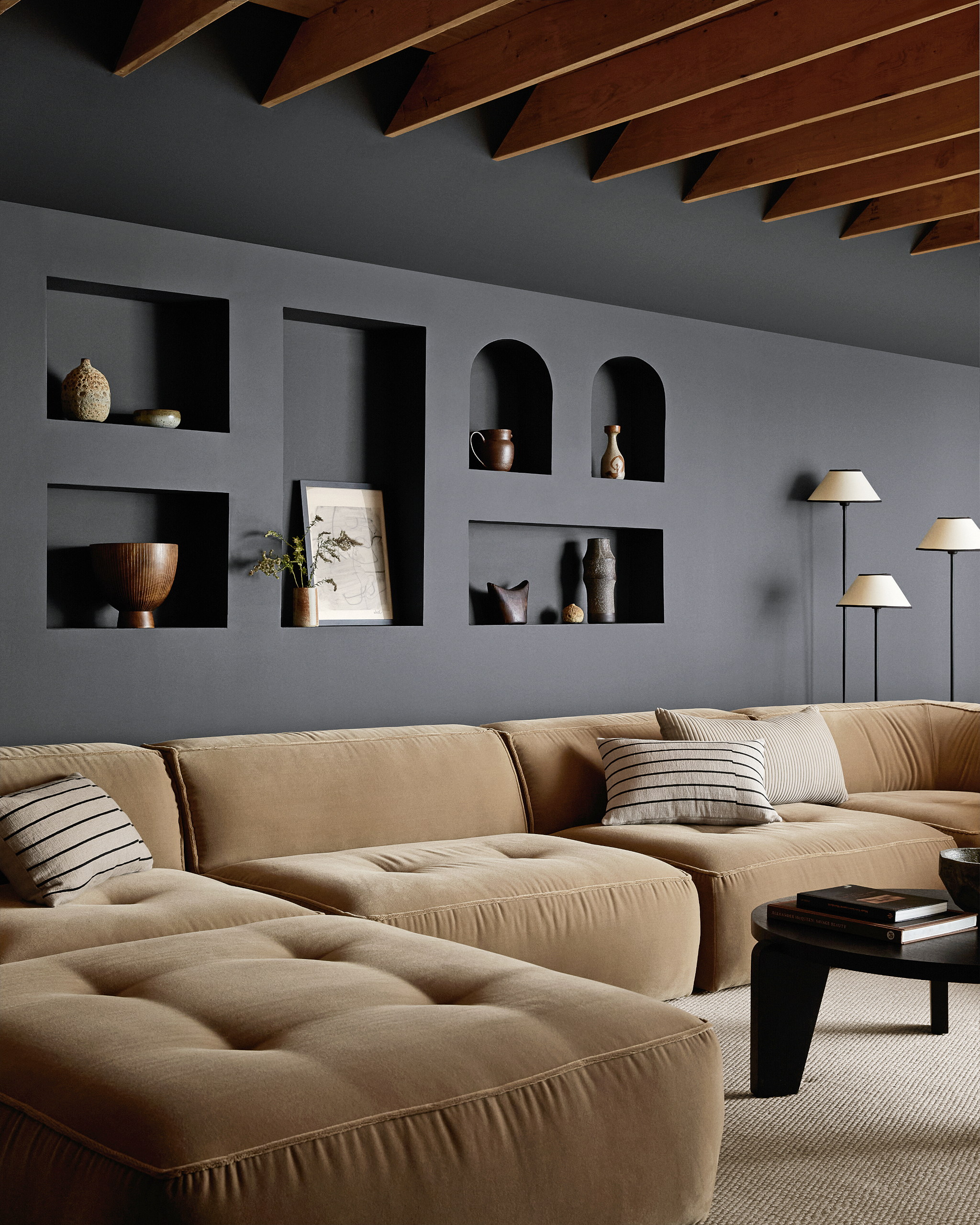 Black snug with alcove shelving, beige corner sofa, beige rug and black round coffee table