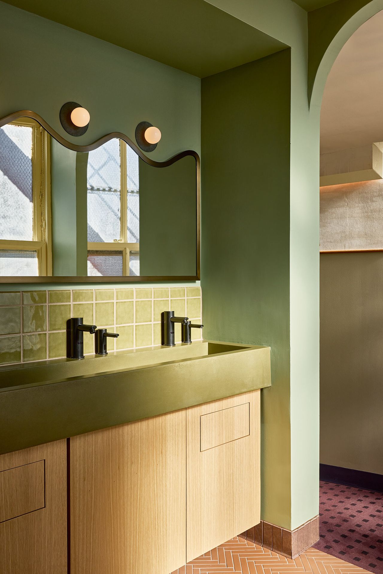 A vibrantly decorated hotel features murals-clad walls in pastel tones, wooden furniture, and Art Deco spherical lighting enriched with a goldeny base.