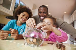 Father with children putting coins into a clear pig money box