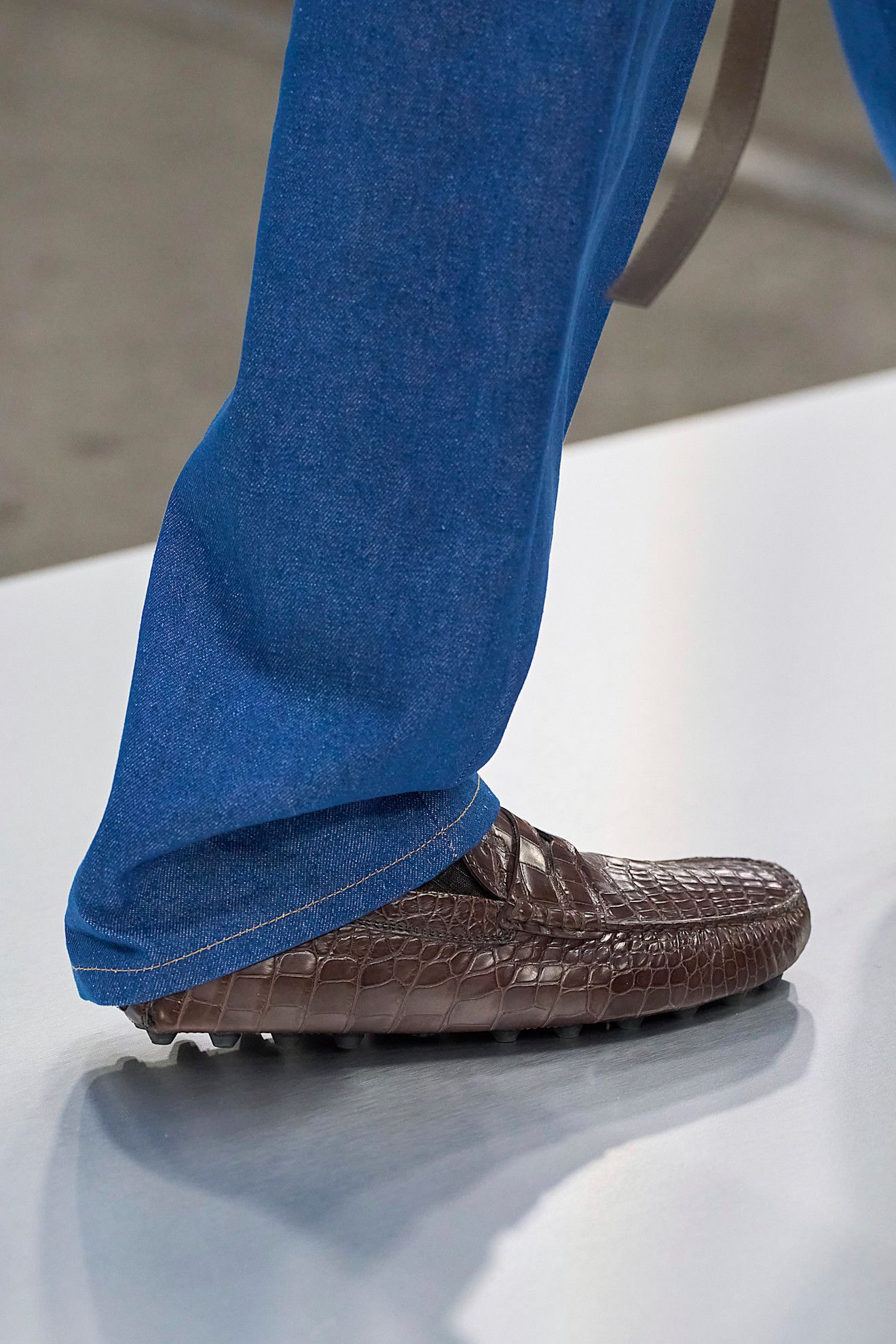 Tods autumn/ winter 2024 runway features a brown shoe outfit. Its a croc brown loafer and blue jeans in an image taken from Launchmetrics.