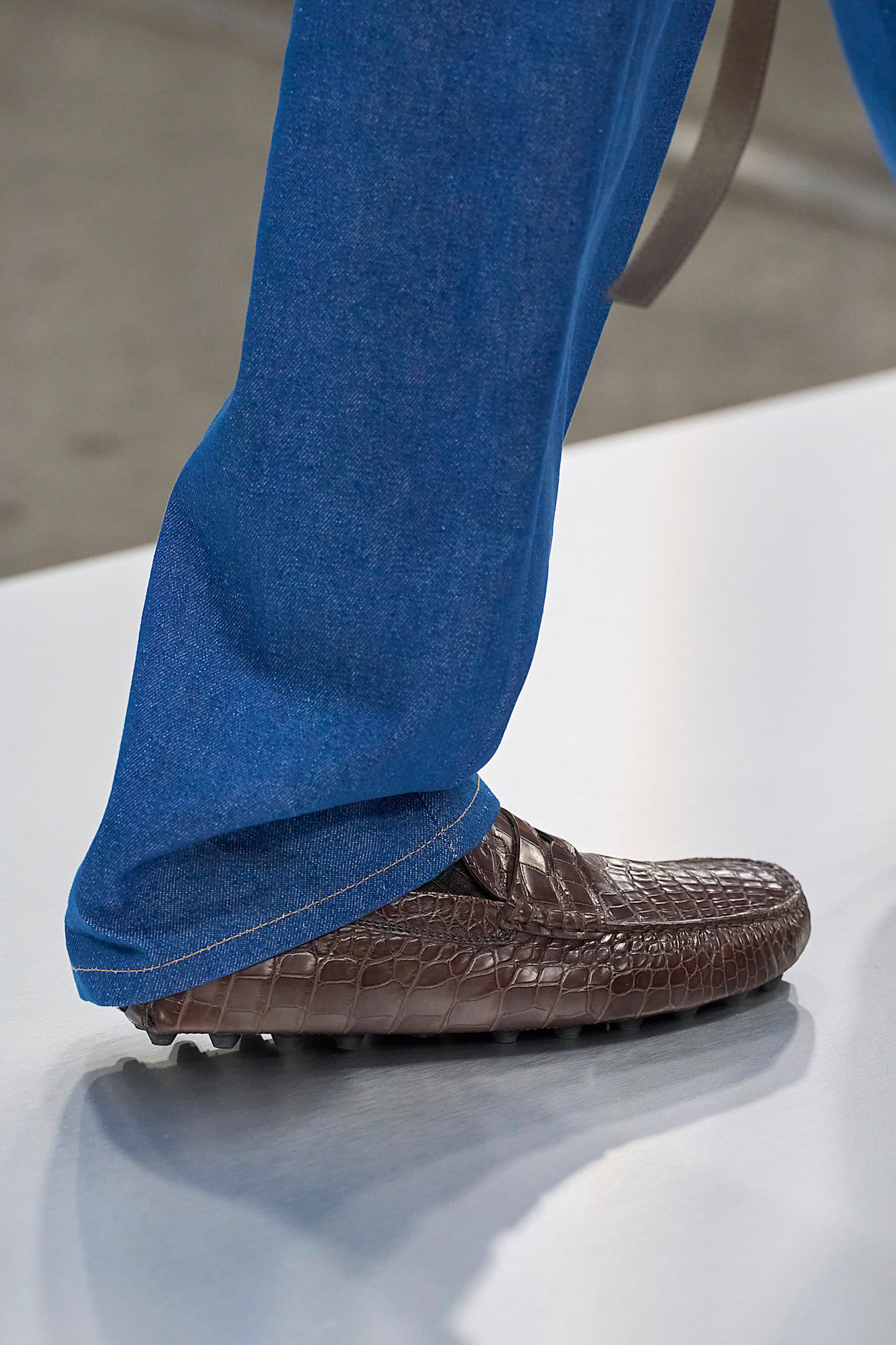Tods autumn/ winter 2024 runway features a brown shoe outfit. Its a croc brown loafer and blue jeans in an image taken from Launchmetrics.