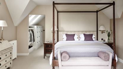 Walk-in closet ideas with white storage solutions, shown beyond a taupe colored bedroom with large four poster bed.