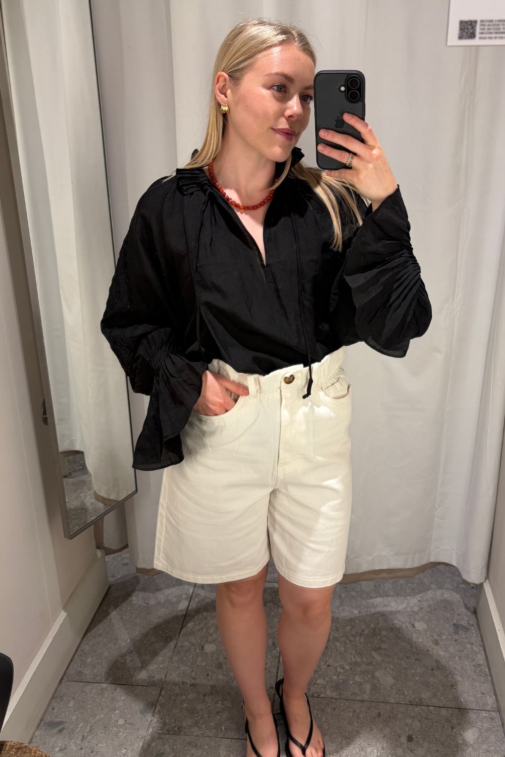 Florrie wears a black blouse, white shorts and black sandals