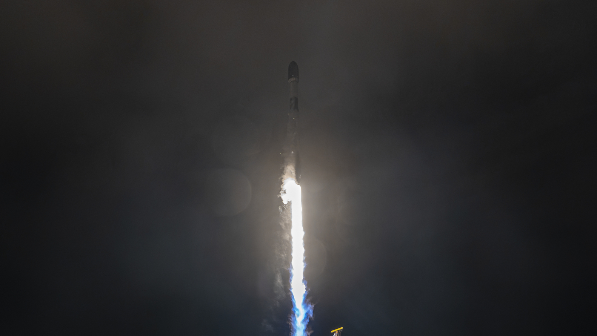 A white rocket blasts off in the dark of night.