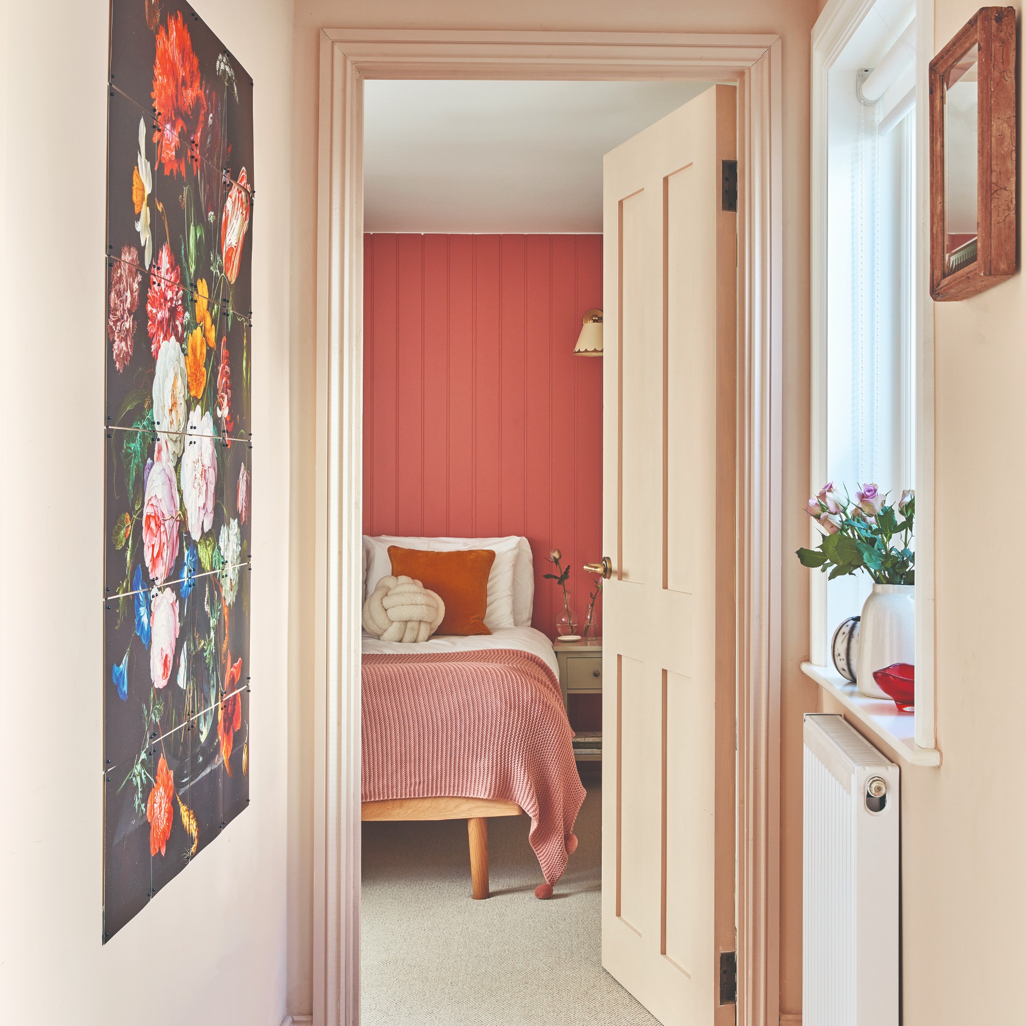 A pink hallway with a floral artwork on the wall leading into the bedroom