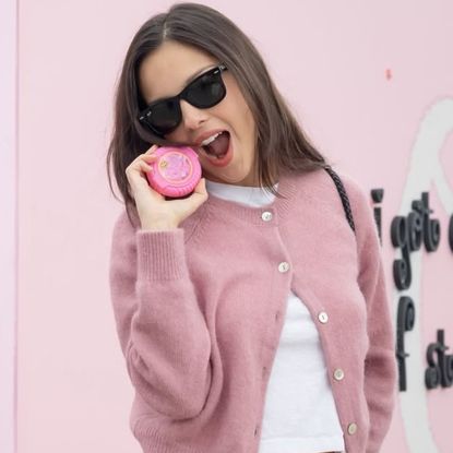 Olivia Rodrigo wears a pink Doen cardigan with blue jeans and a white T-shirt and carries a black woven bag