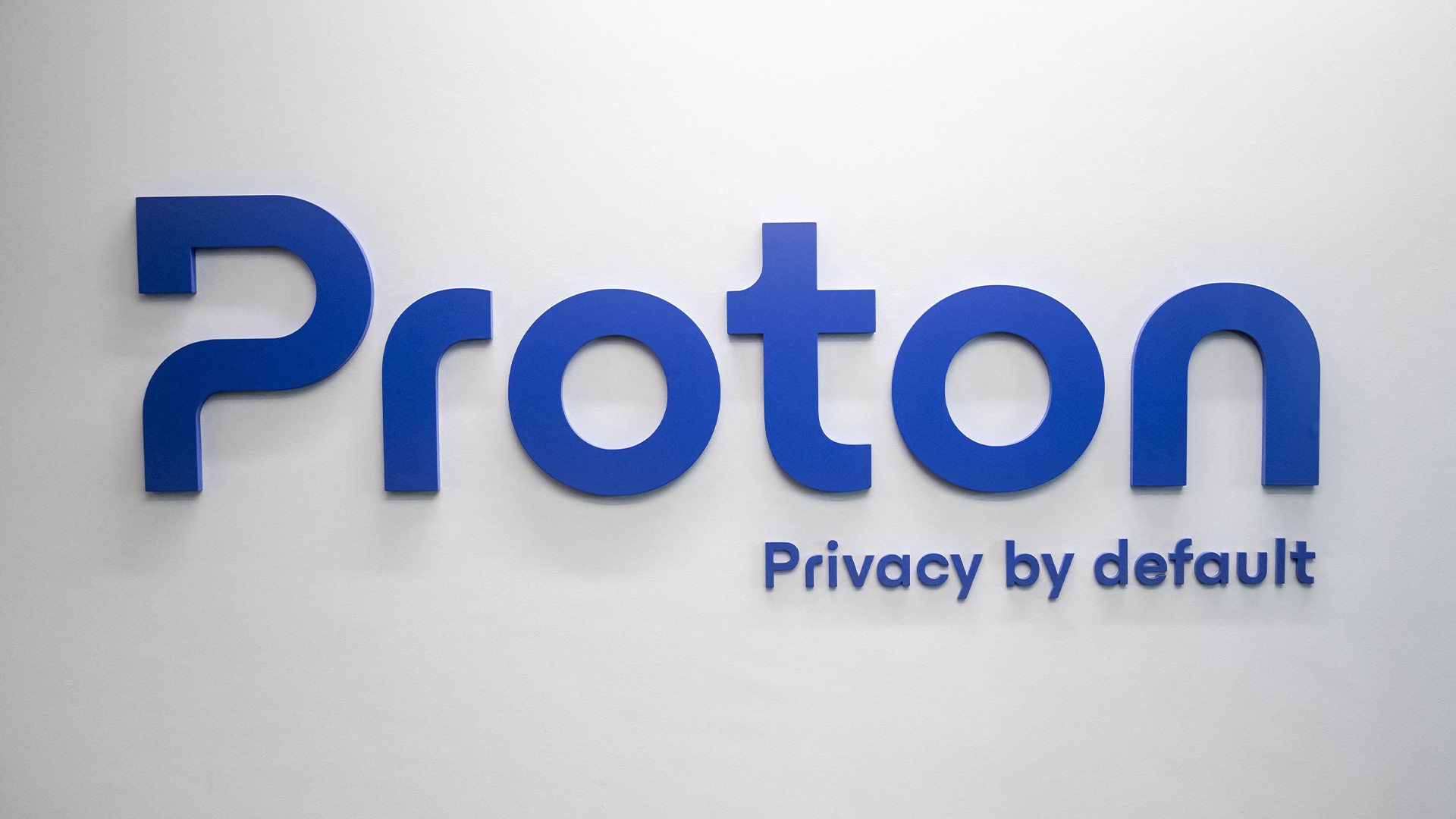 Proton logo and branding, including 'Privacy by Default' term, pictured in blue lettering on a white wall.