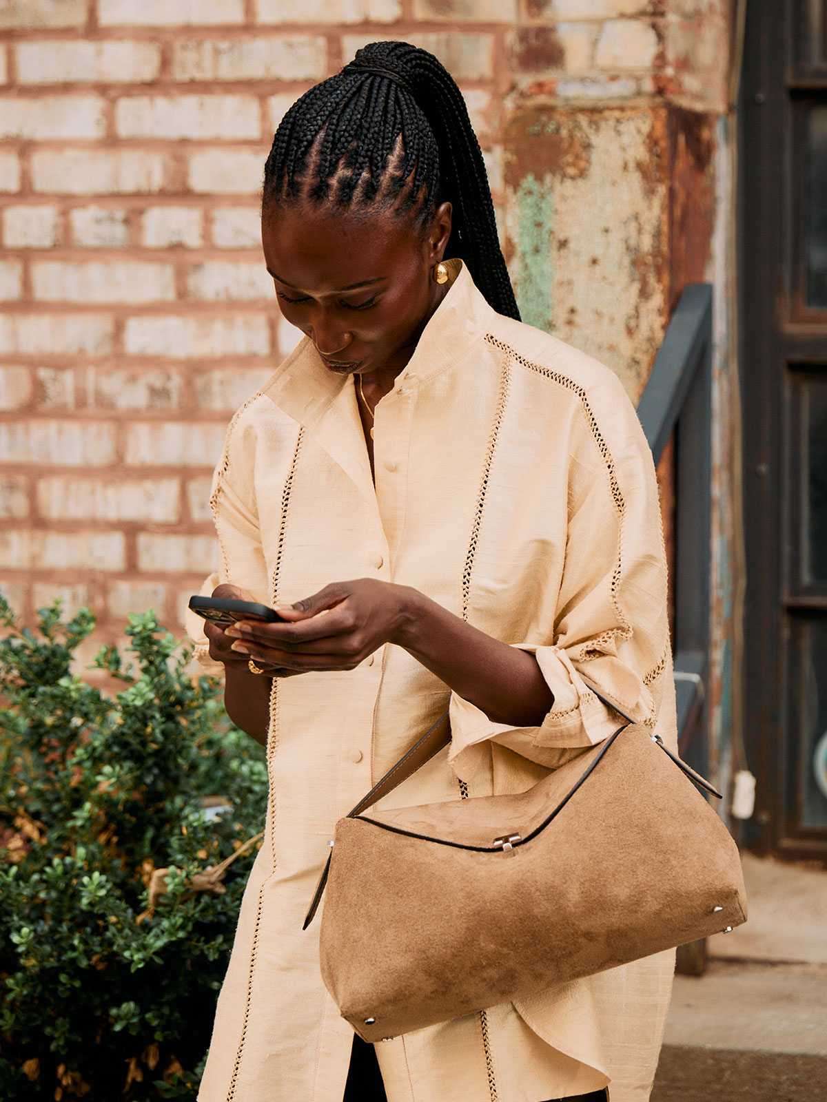 Woman wearing a tan button-down and tan suede Toteme handbag.