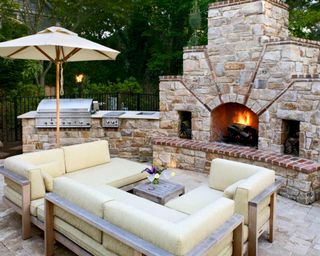 An outdoor bbq area with a stone fireplace and patio sofa set
