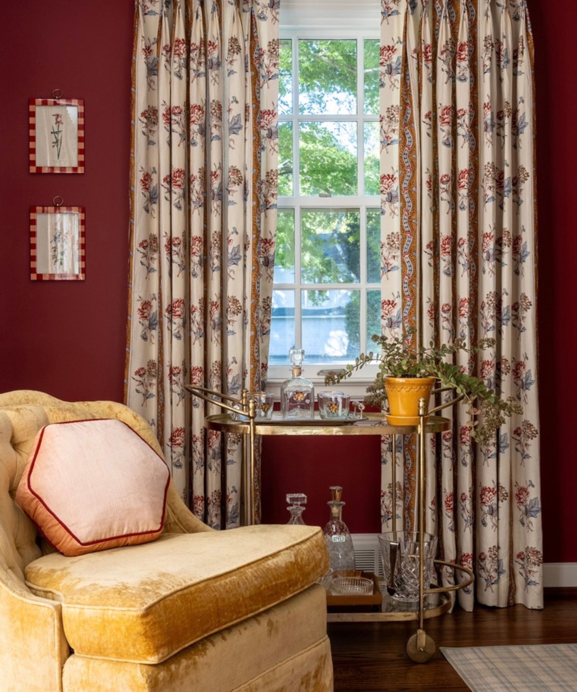 a rich red painted living room with floral curtains, a yellow velvet armchair and a styled bar cart