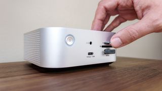 A person inserting a microSD card into a card reader on the front of the Satechi Thunderbolt 5 CubeDock on a desk