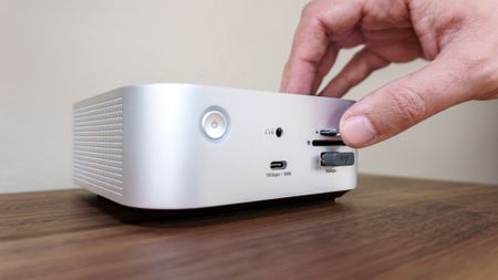 A person inserting a microSD card into a card reader on the front of the Satechi Thunderbolt 5 CubeDock on a desk