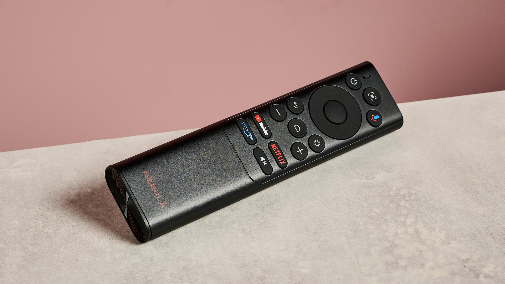 The Anker Nebula Cosmos 4K SE's remote control sits on a stone-effect surface with a pink background.