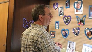 Reverend Richard Coles in a checked shirt looks at a wall full of photos of peoples' late loved ones.