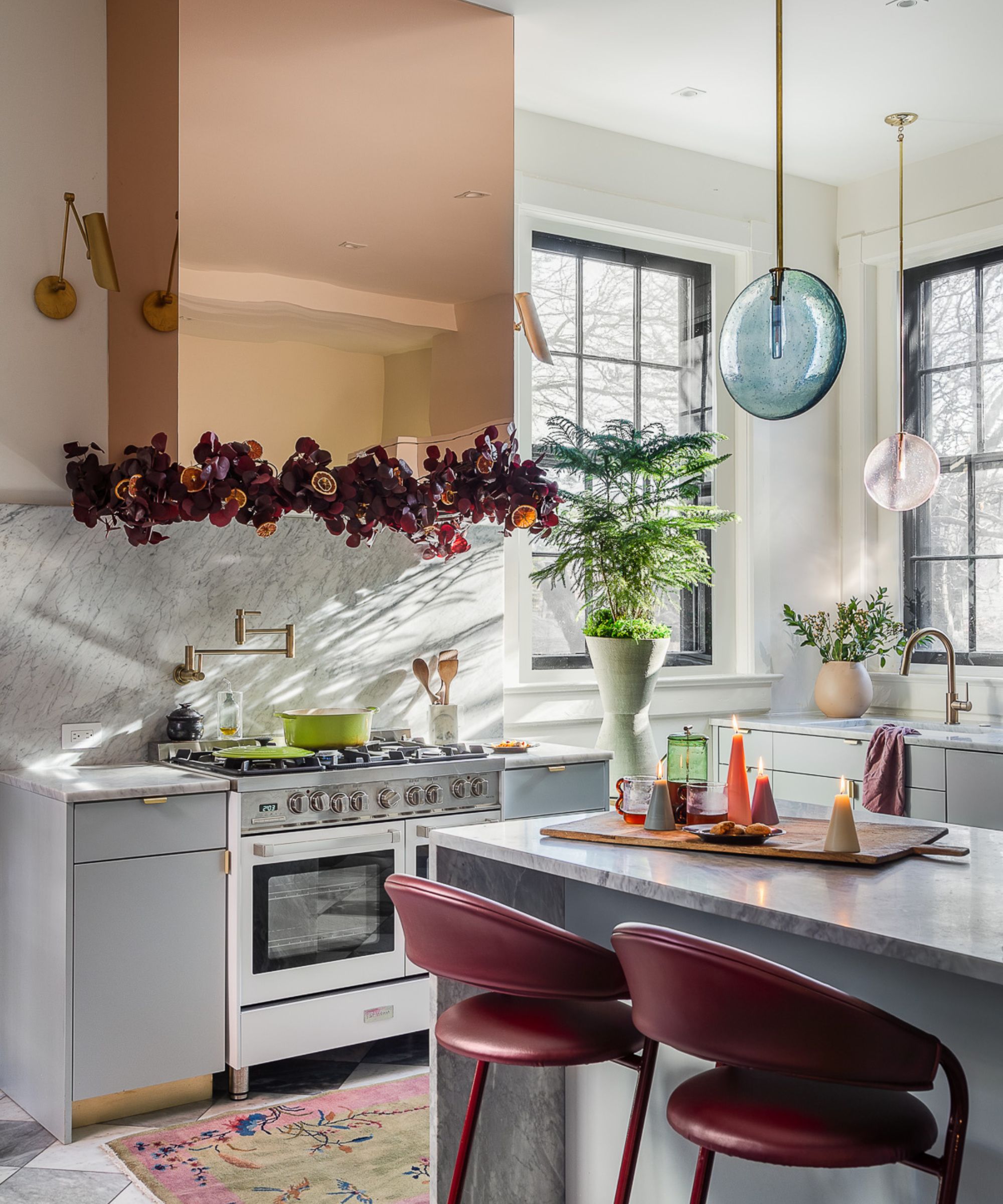 A blue and white kitchen decorated for winter with seasonal foliage, layered lighting, and colorful candles