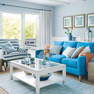 Living room with sofa in bright blue, pale blue walls, rug in pale blue, white ceiling and white table