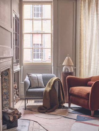Armchairs beside a fireplace with a large sash window behind.