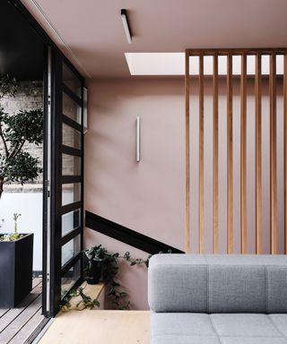 rose pink living room with gray modular couch, blond wood floor, black crittall window:door, view of outside