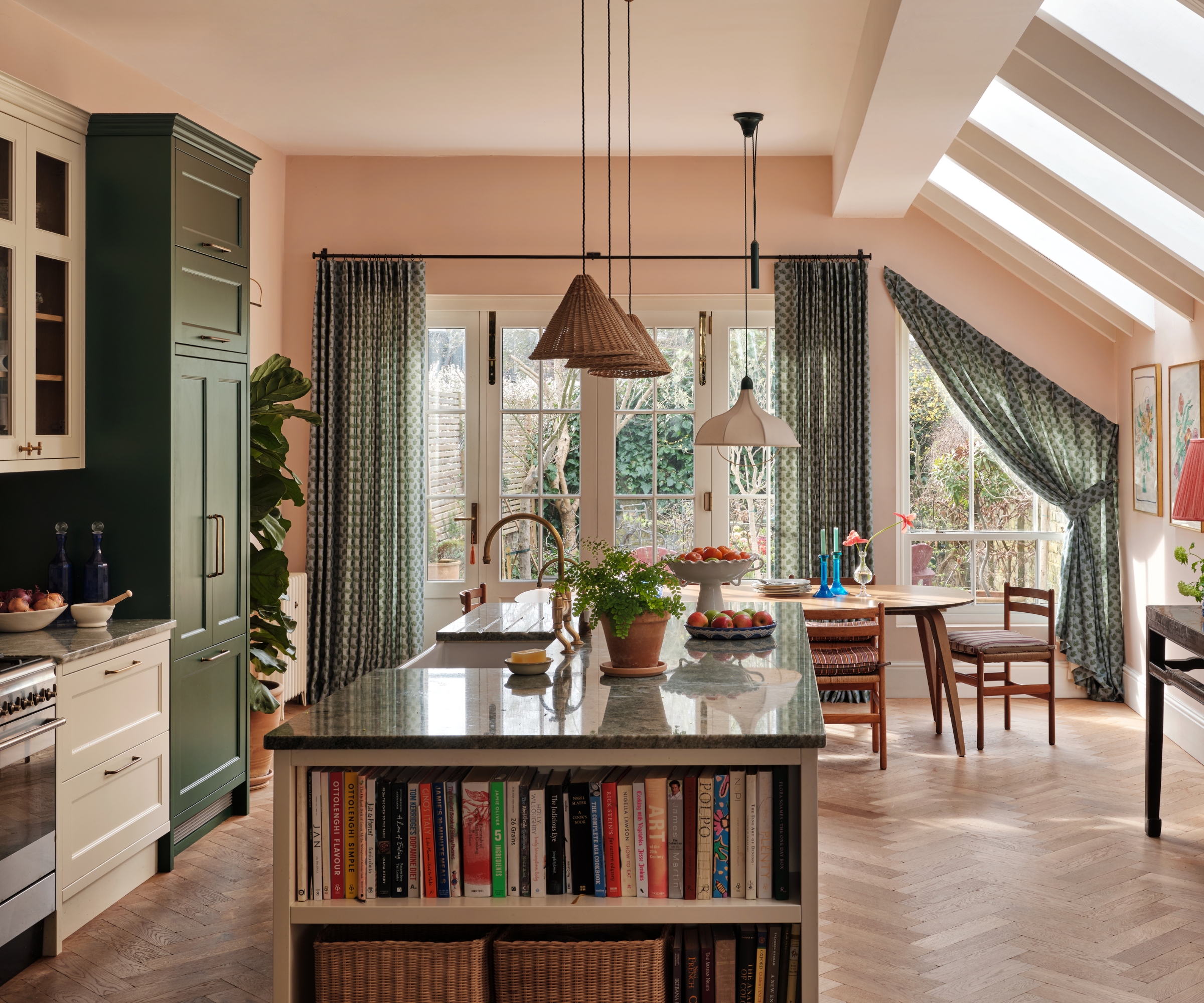 An open plan kitchen with green countertops, white and green cabinets, wood floors, and an oval wood dining table, and green curtains