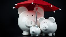 A three-member piggy bank "family" under a red umbrella.