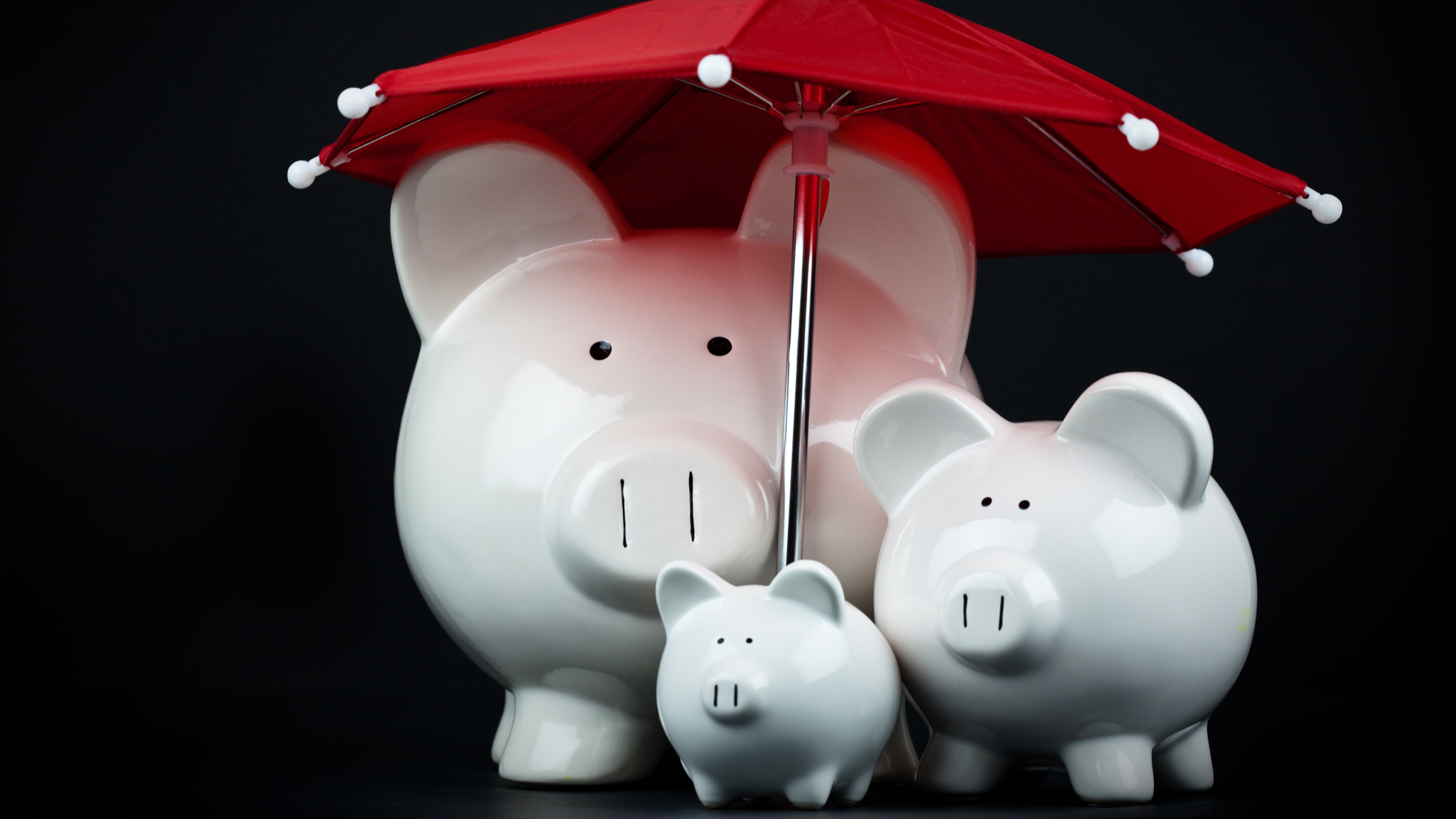 A three-member piggy bank "family" under a red umbrella.