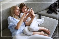 Mother and daughter sitting on sofa looking at shared smartphone