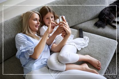 Mother and daughter sitting on sofa looking at shared smartphone