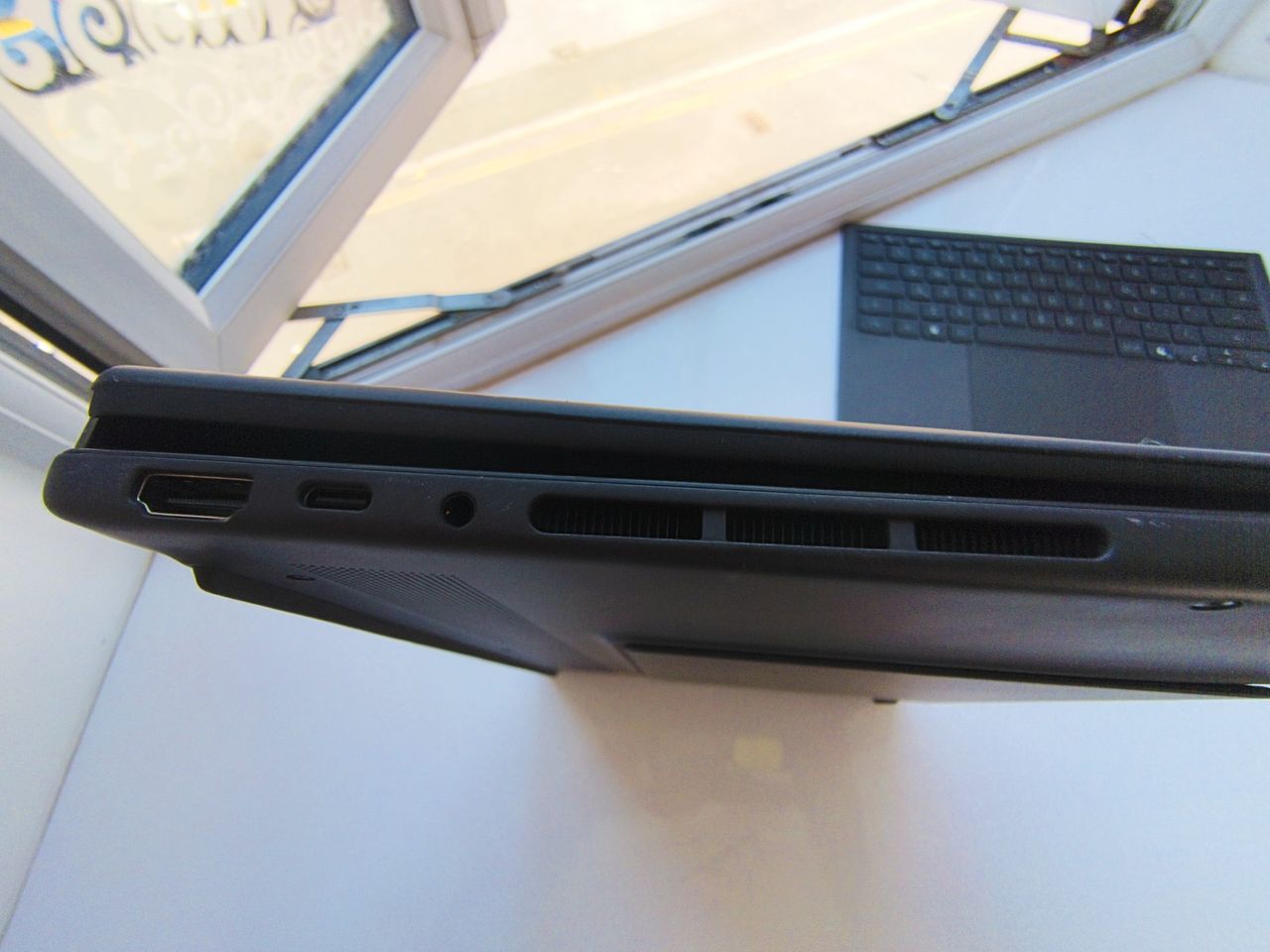 Side angle view of the ASUS Zenbook Duo in traditional laptop mode, displaying the Windows lock screen showing the time 15:52 against a mountain landscape background next to an open window.