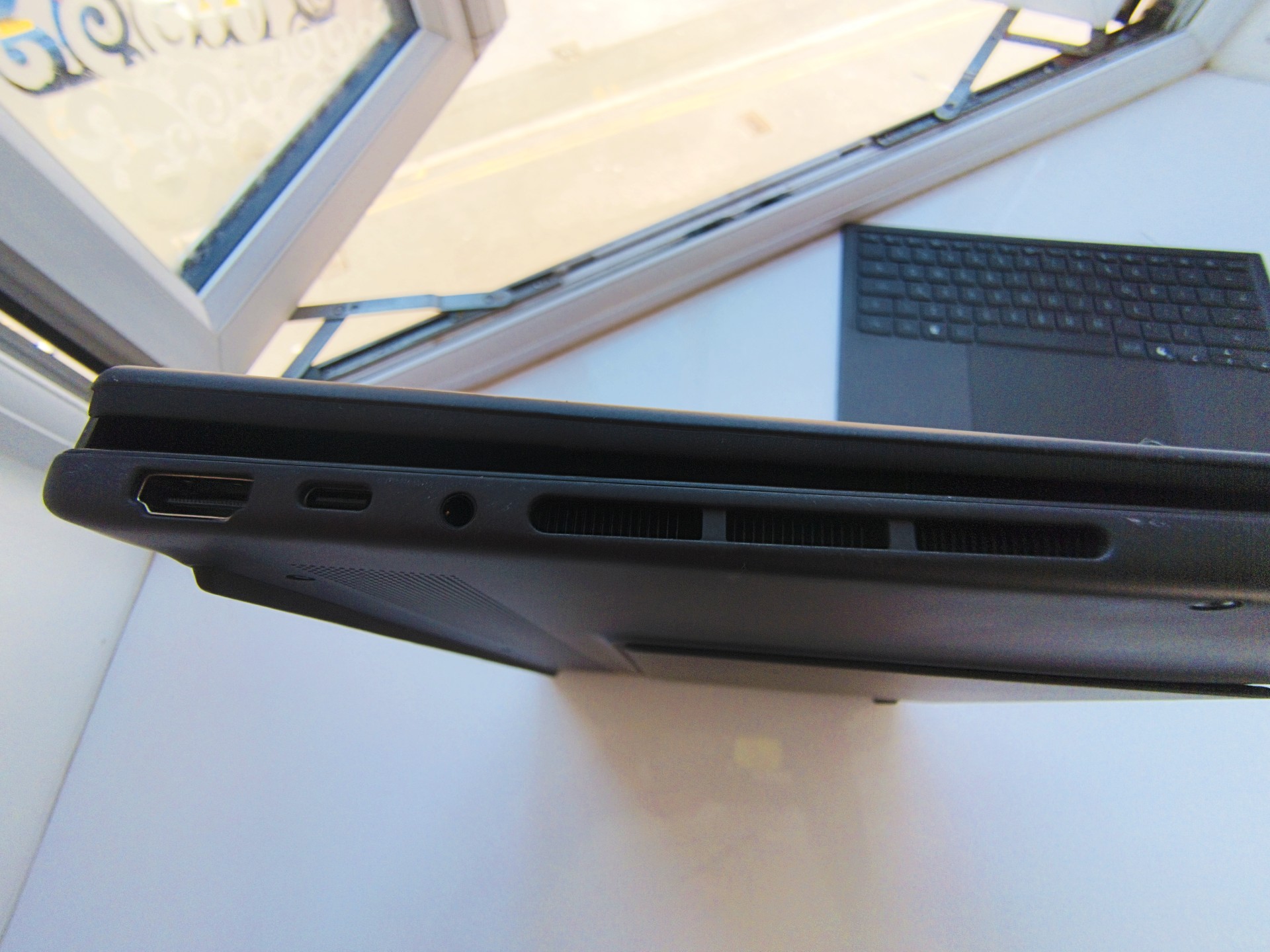 Side angle view of the ASUS Zenbook Duo in traditional laptop mode, displaying the Windows lock screen showing the time 15:52 against a mountain landscape background next to an open window.